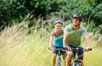 Ein Paar fährt mit dem Fahrrad über eine Wiese mit sehr langem Gras